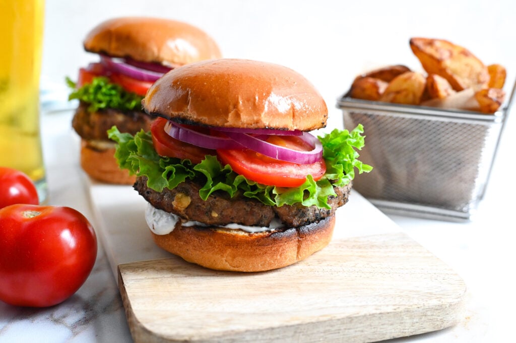 Delicious Greek-style grilled lamb burgers with feta topped with tzatziki, tomatoes, lettuce and red onions.