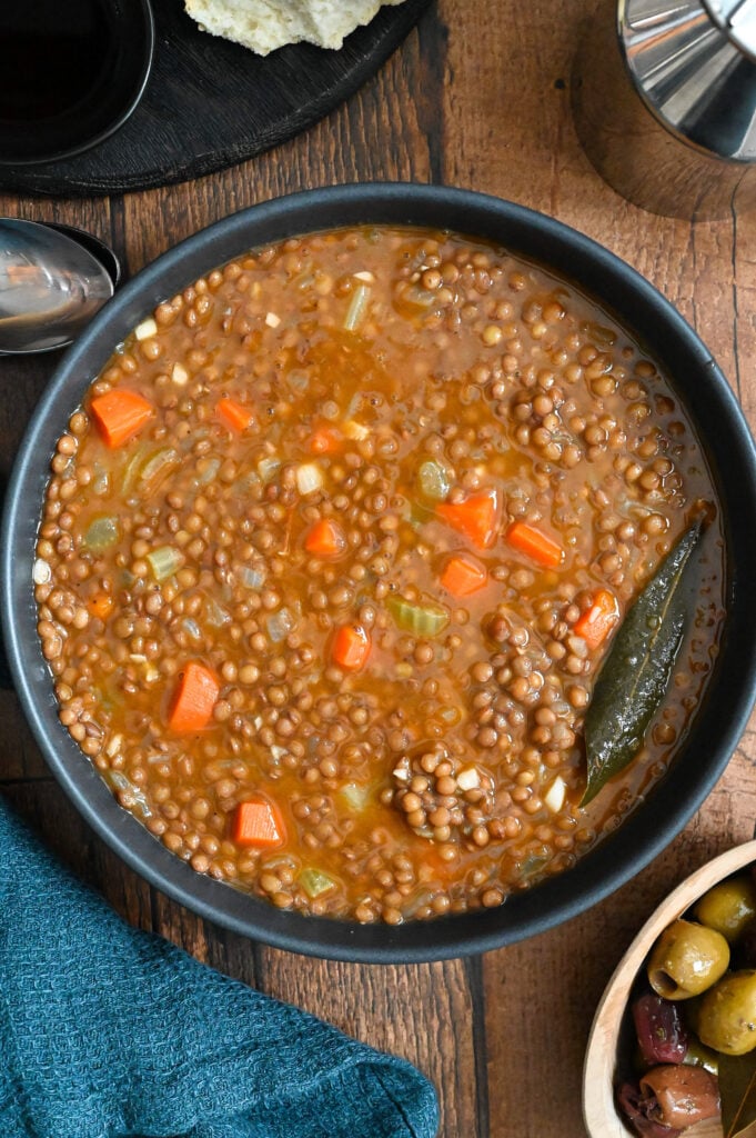 Fakes (Lentil soup) are served in a black bowl pictured with bread and olives.