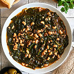 Black-eyed peas and spinach, in a white bowl, pictured with bread and olives