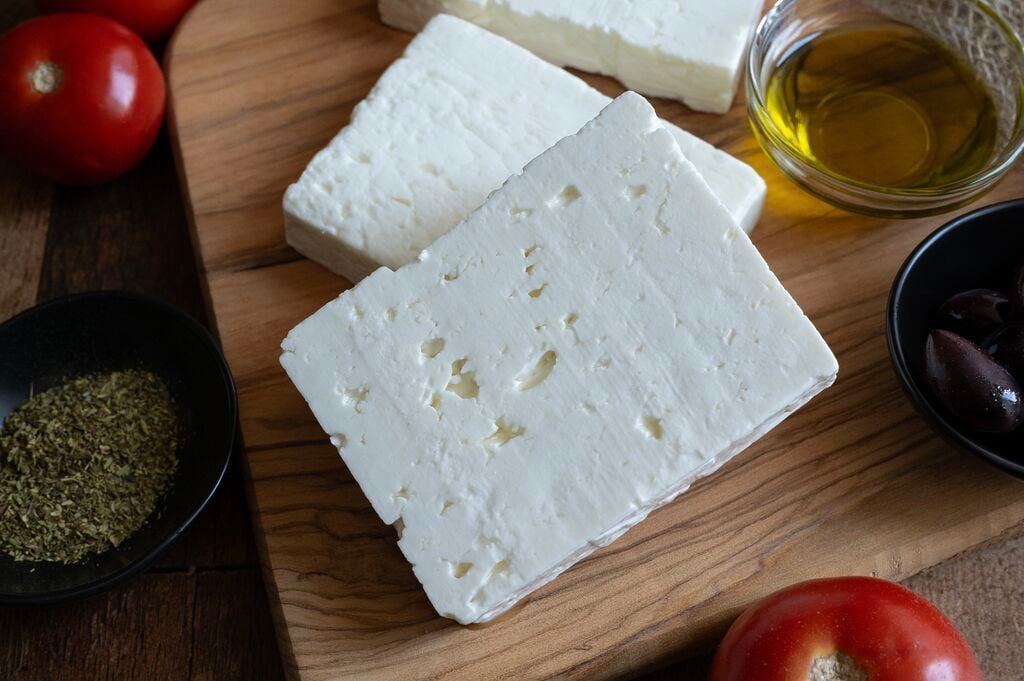 Blocks of feta cheese on a wooden board, surrounded by olive oil, olives, and oregano.