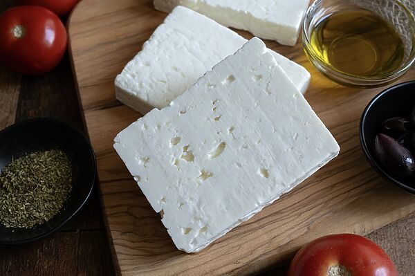 Blocks of feta cheese on a wooden board, surrounded by olive oil, olives, and oregano.