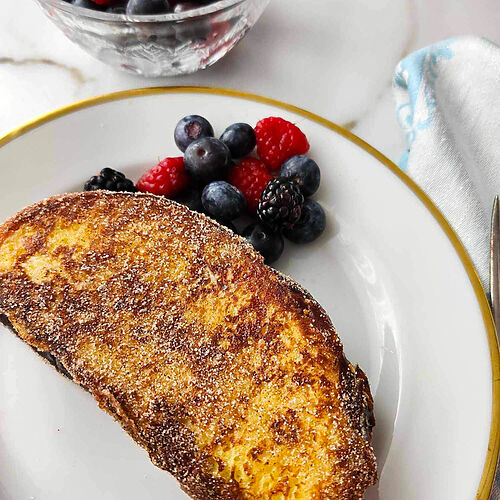 Tsoureki French toast sandwich with cream cheese and jam, on a white plate, and fresh berries on the plate.