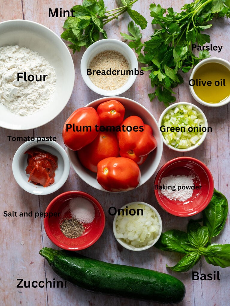 Ingredients for the tomato fritters which include: Plum or Roma tomatoes; flour, breadcrumbs, mint, parsley, basil, olive oil, green onion, yellow onion, zucchini, salt and pepper, baking powder and tomato paste