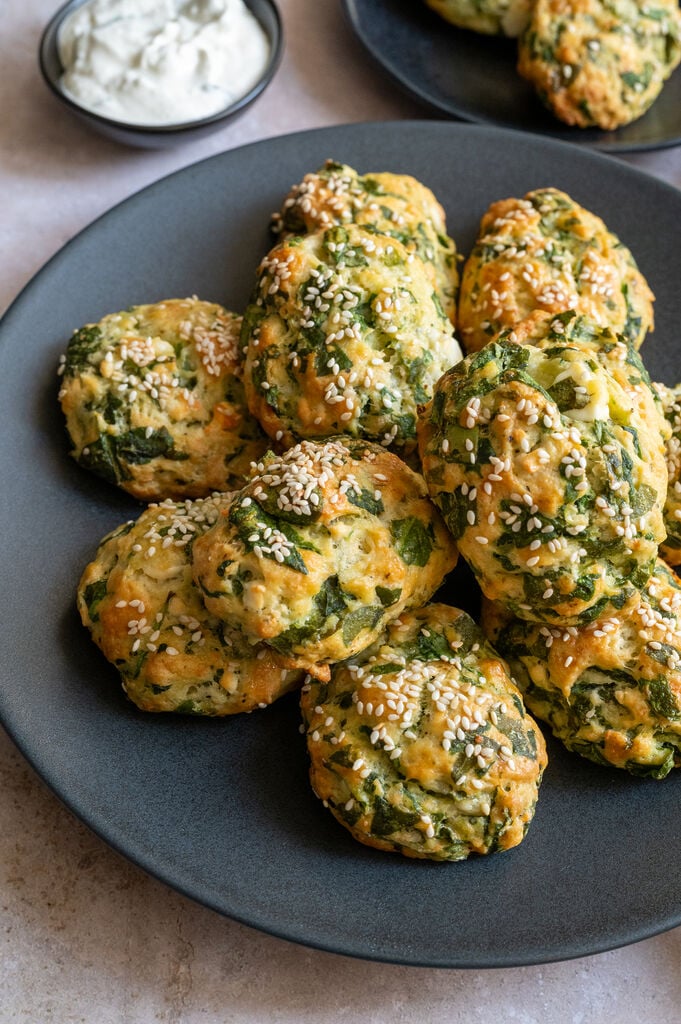 Greek Spanakotiropitakia (spinach and cheese pita) without phyllo, on a black plate surrounded by feta and olives.