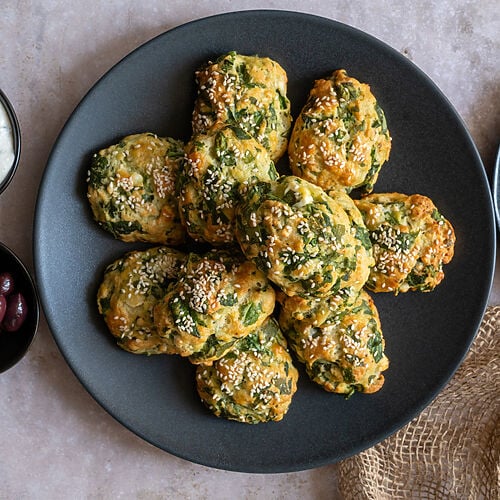 Greek Spanakotiropitakia (spinach and cheese pita) without phyllo, on a black plate surrounded by feta and olives.