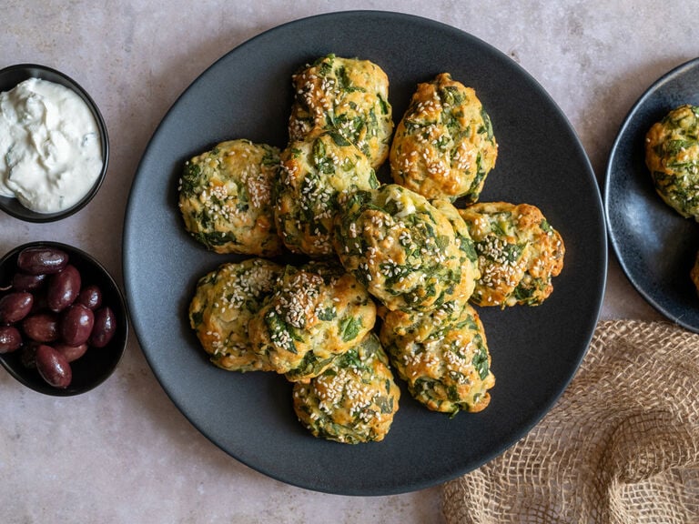 Greek Spanakotiropitakia (spinach and cheese pita) without phyllo, on a black plate surrounded by feta and olives.