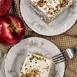 A piece of the cake on a white plate surrounded by apples.