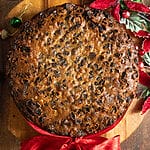 Fruitcake on a wood platter with a red ribbon around it.