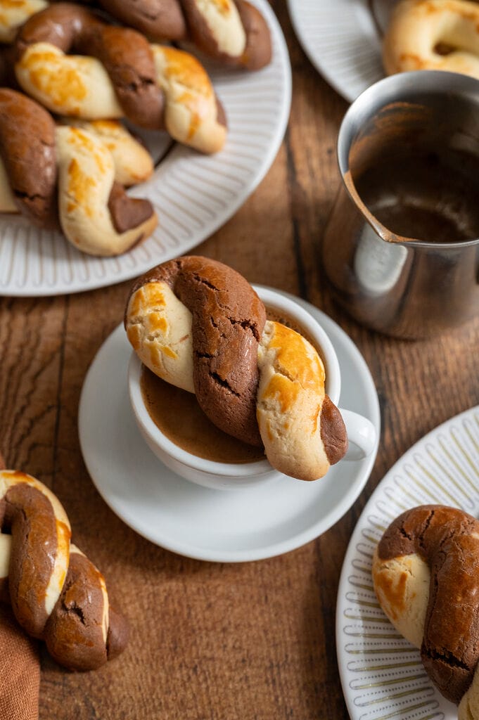 Greek butter koulourakia with a chocolate twist sitting on top of the cup of Greek coffee.