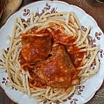 Rooster with pasta and tomato sauce (Kokora kokkinisto me makaronia) on a white platter with brown flowers on it.