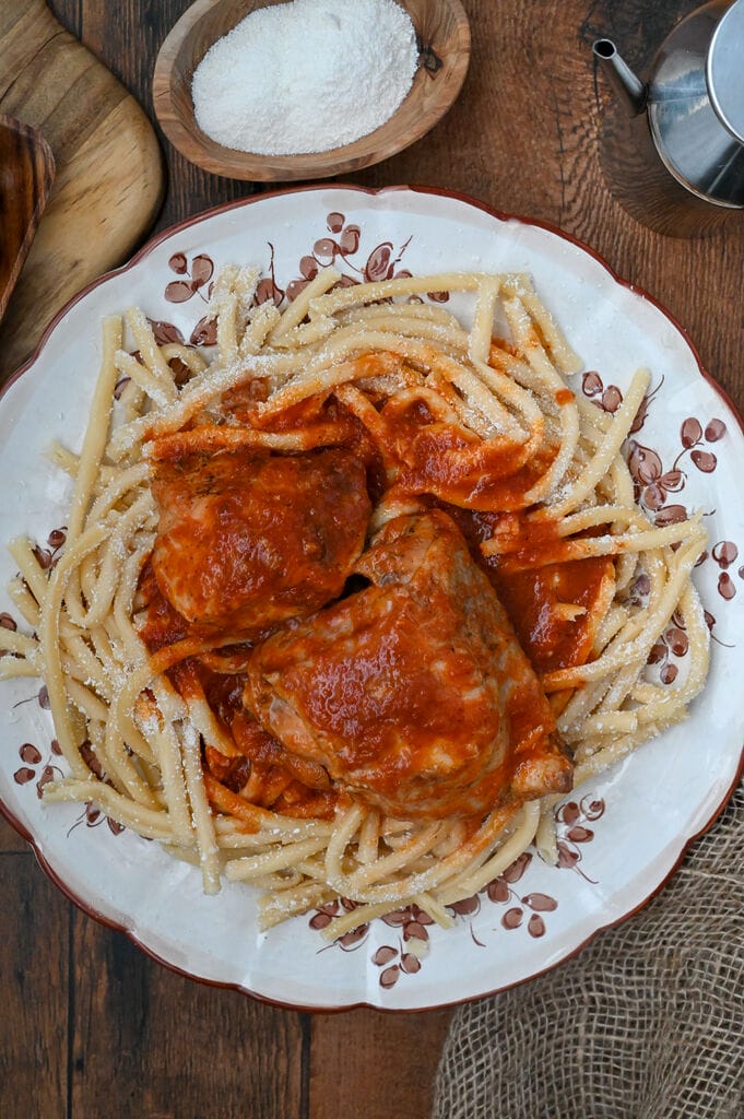 Rooster with pasta and tomato sauce (Kokora kokkinisto me makaronia) on a white platter with brown flowers on it.