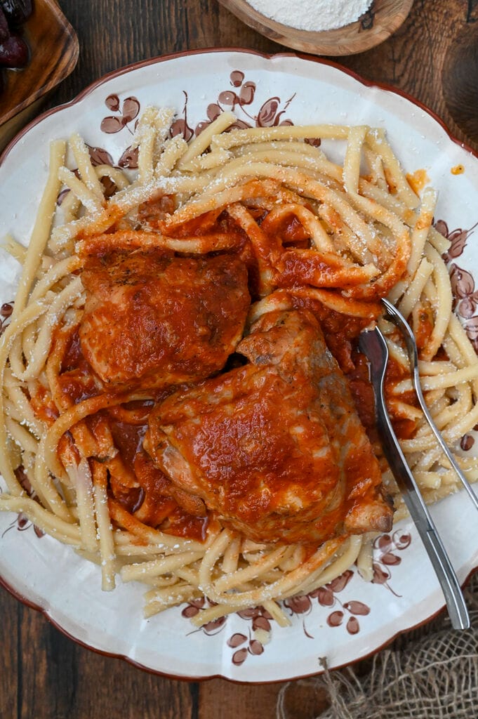Rooster with pasta and tomato sauce (Kokora kokkinisto me makaronia) on a white platter with brown flowers on it.