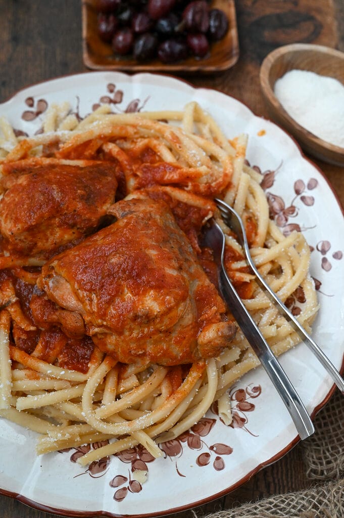 Rooster with pasta and tomato sauce (Kokora kokkinisto me makaronia) on a white platter with brown flowers on it.