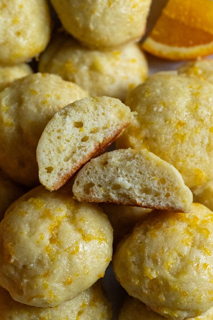 Orange ricotta cookies on a tray, and one of them is cut up.