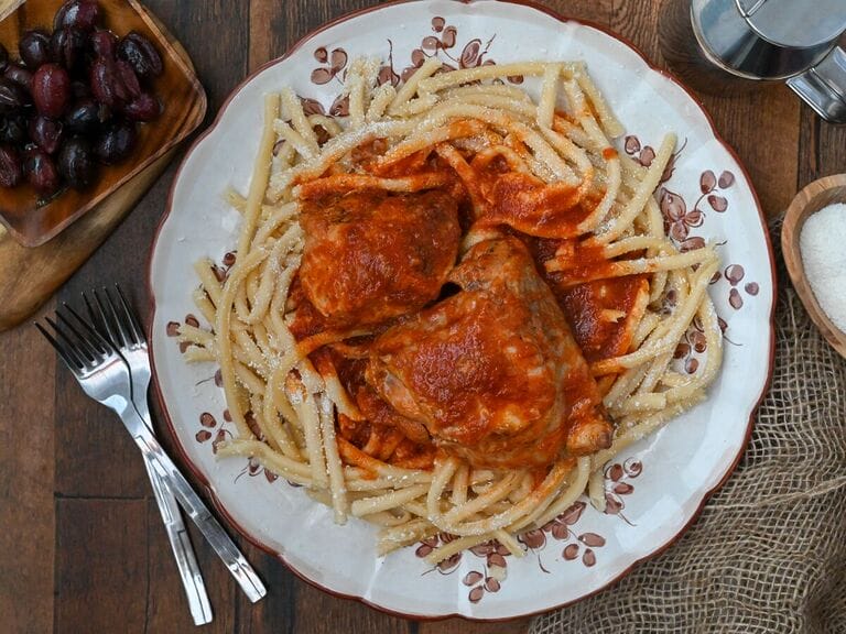 Rooster with pasta and tomato sauce (Kokora kokkinisto me makaronia) on a white platter with brown flowers on it.