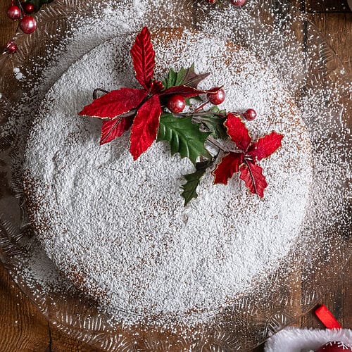 Vasilopita or Greek New Year Cake (Βασιλόπιτα), on a glass platter surrounded by Christmas decorations.