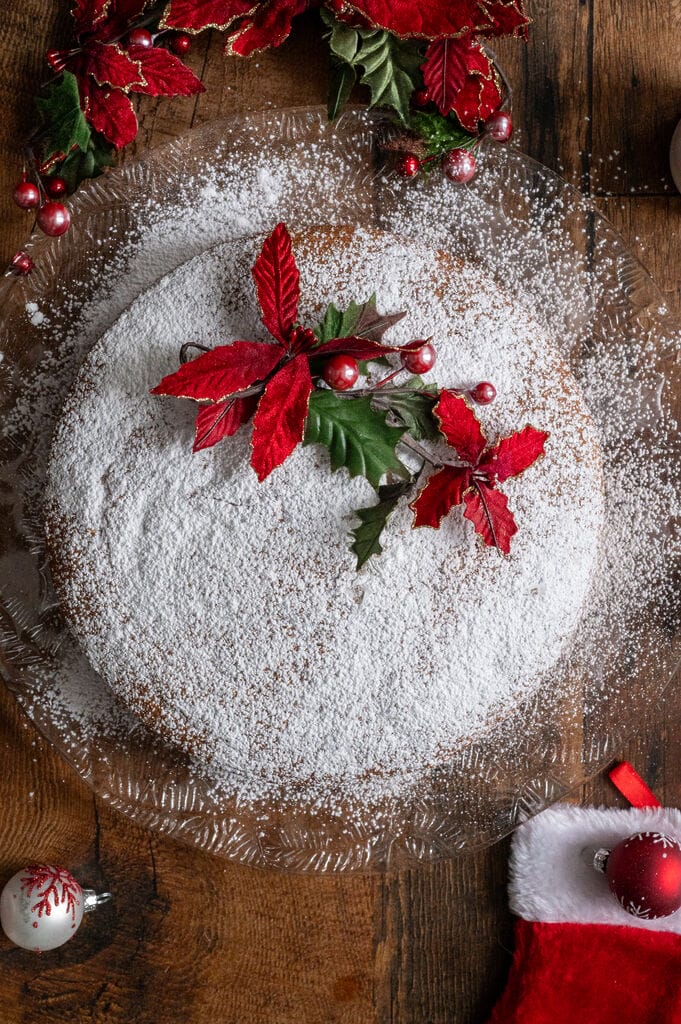 Vasilopita or Greek New Year Cake (Βασιλόπιτα), on a glass platter surrounded by Christmas decorations.