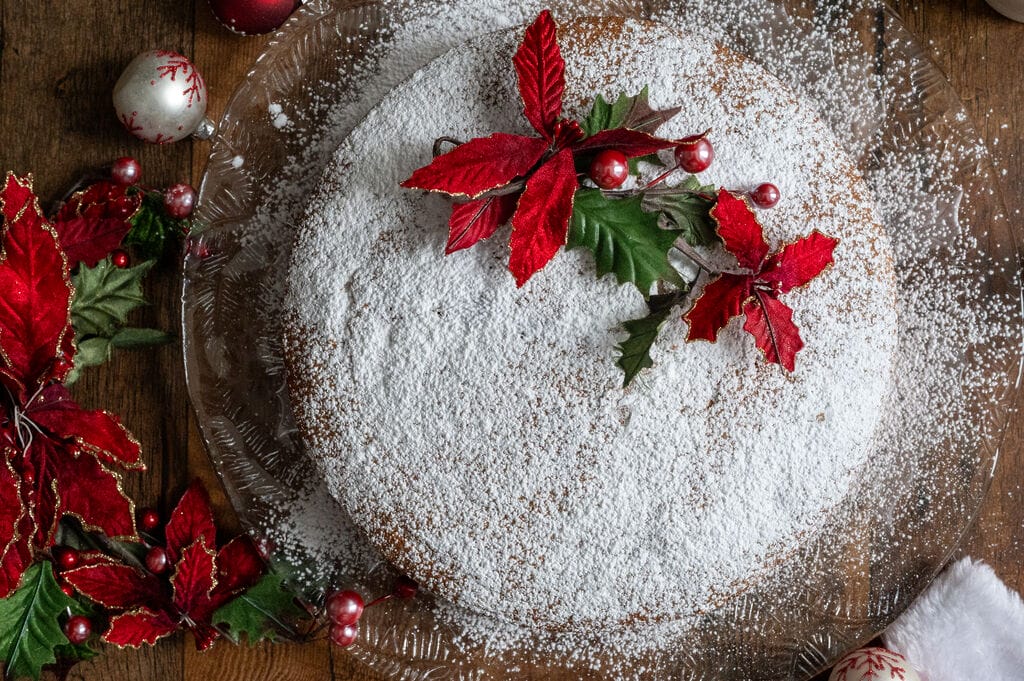 Vasilopita or Greek New Year Cake (Βασιλόπιτα), on a glass platter surrounded by Christmas decorations.