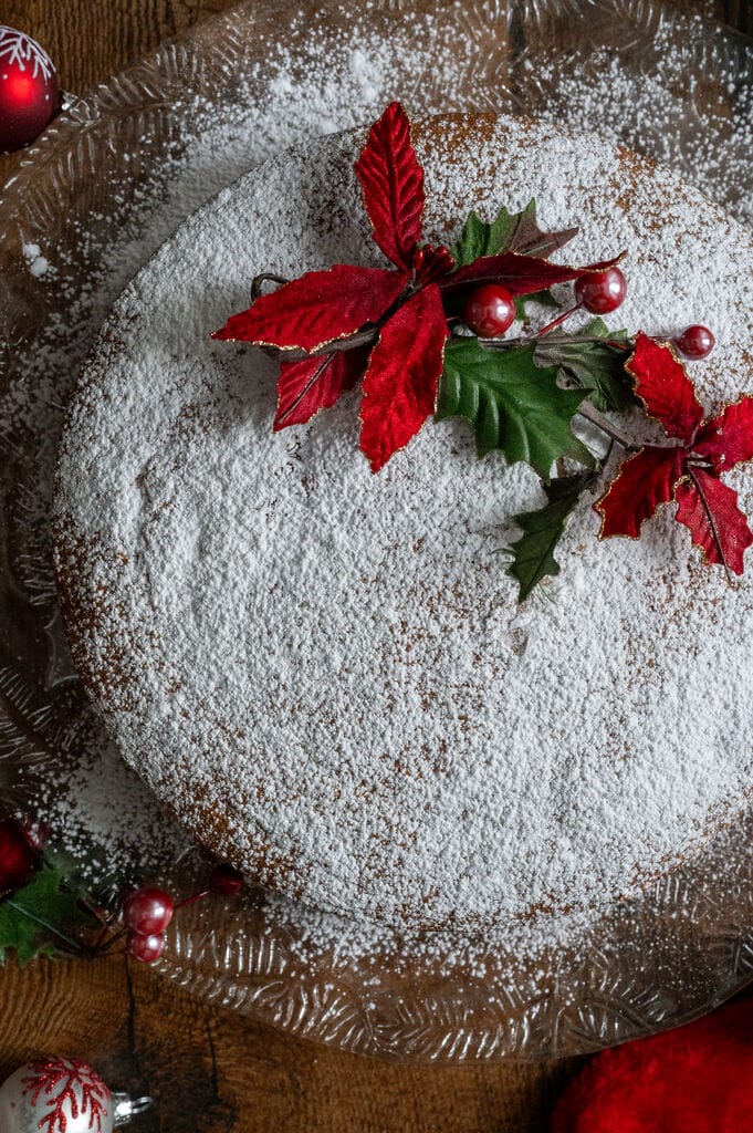 Vasilopita or Greek New Year Cake (Βασιλόπιτα), on a glass platter surrounded by Christmas decorations.