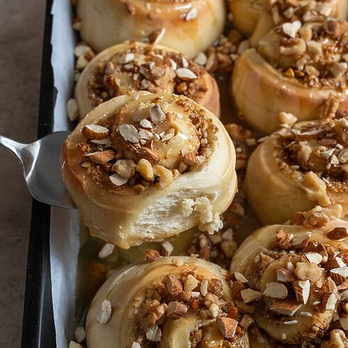 Removing a cinnamon bun from the baking tray.