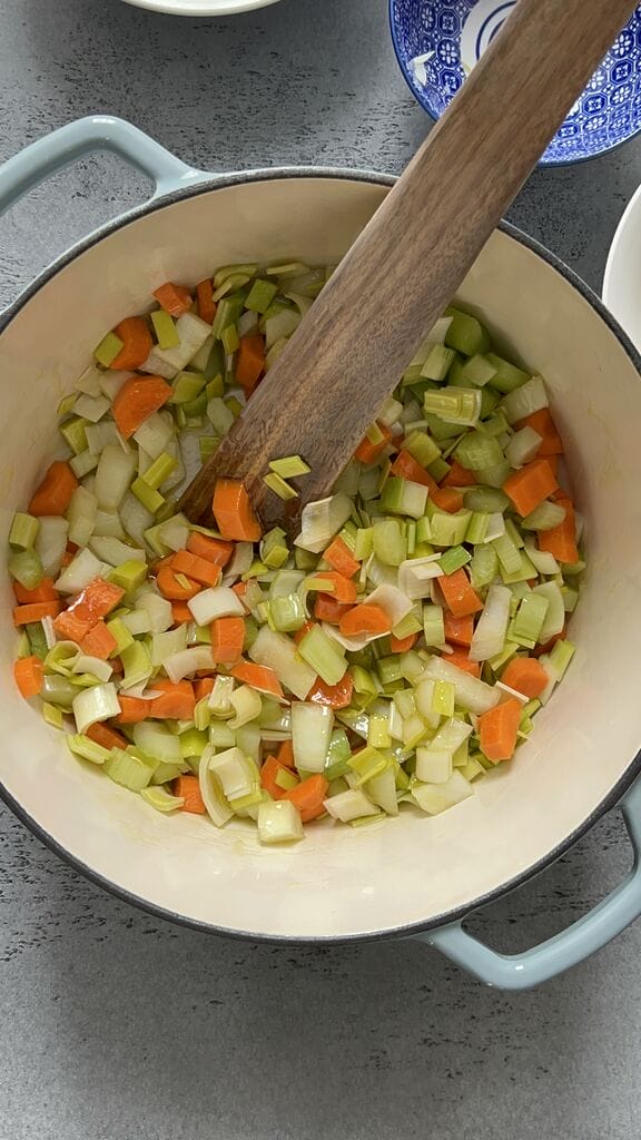 Sautéing the vegetables in a blue cast iron pot.