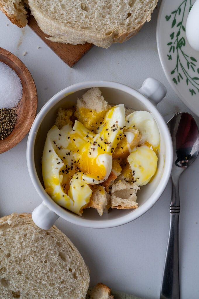 Soft boiled egg in a cup, with cubes of bread, in a white bowl.