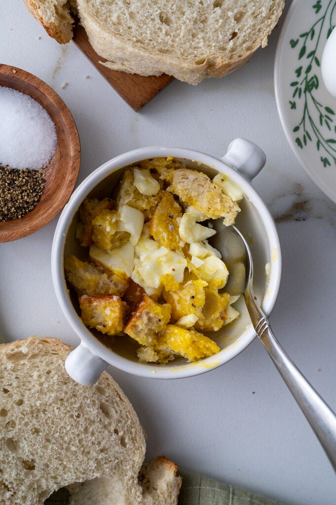 Soft boiled egg in a cup, with cubes of bread, in a white bowl.