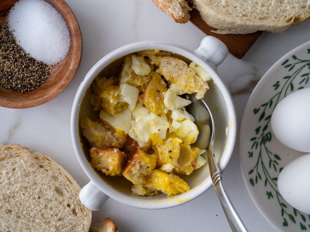 Soft boiled egg in a cup, with cubes of bread, in a white bowl.