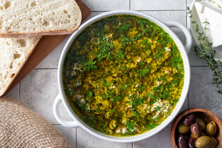 The olive oil dip in a white bowl surrounded by olives and bread.