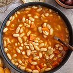 Fasolatha (Fasolada) with tomato sauce soup in a black bowl surrounded by bread, and olives.