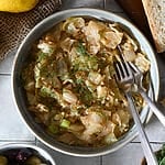 Lahanorizo, a Greek cabbage and rice meal plated in a bowl surrounded by lemons, bread and olives, and sprinkled with some dill.