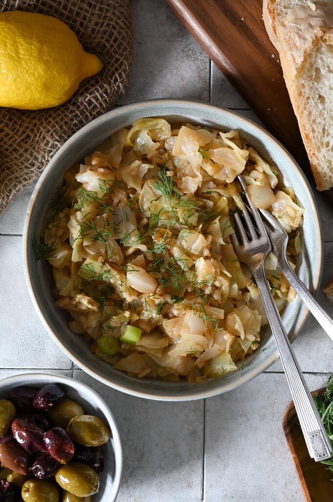 Lahanorizo, a Greek cabbage and rice meal plated in a bowl surrounded by lemons, bread and olives, and sprinkled with some dill.