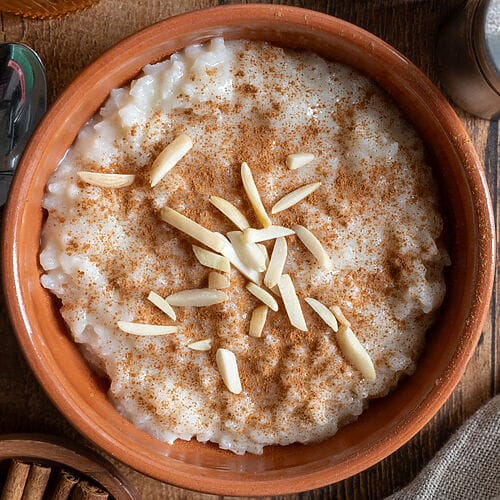 Rice pudding in a brown bowl topped with ground cinnamon and slivered almonds.