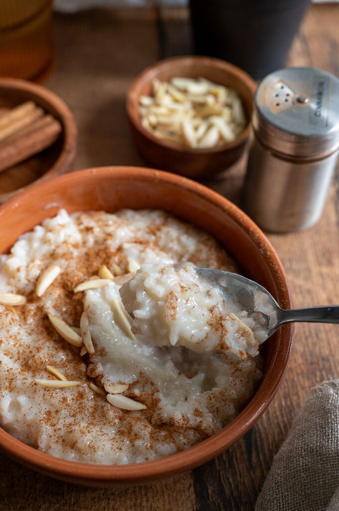 Rice pudding in a brown bowl topped with ground cinnamon and slivered almonds.