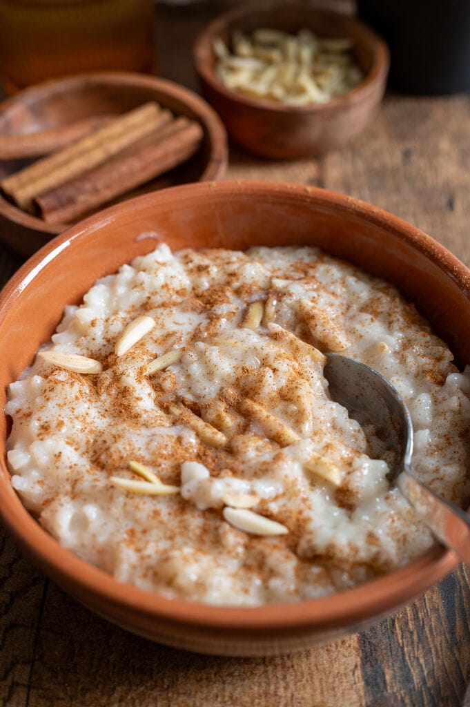 Rice pudding in a brown bowl topped with ground cinnamon and slivered almonds.