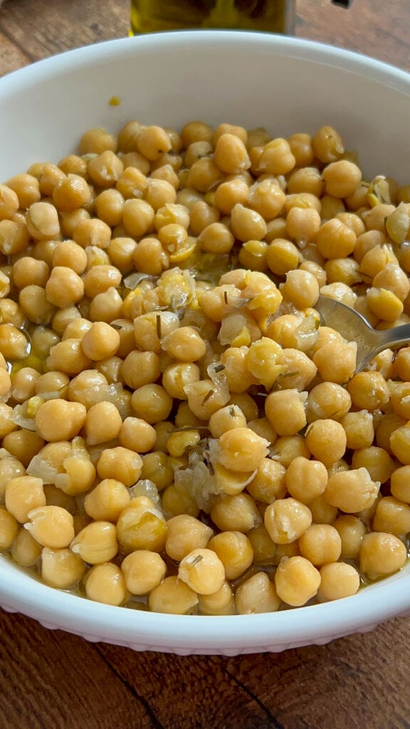 Baked chickpeas in a white bowl, surrounded by bread, and olives.