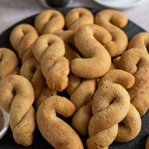 Olive oil koulourakia with orange and cinnamon on a brown wooden board.