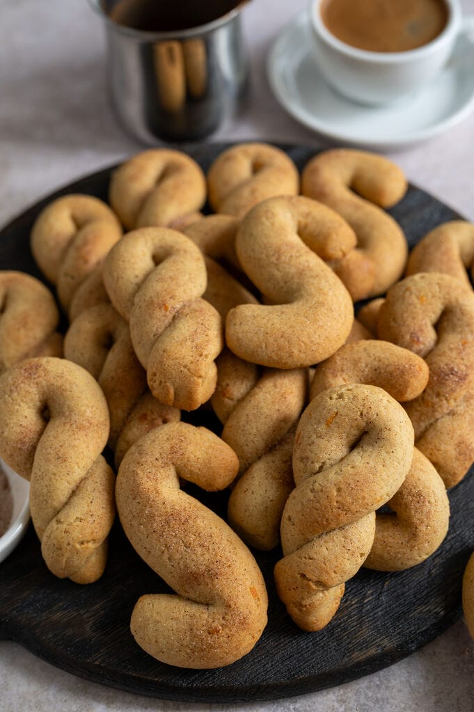 Olive oil koulourakia with orange and cinnamon on a brown wooden board.