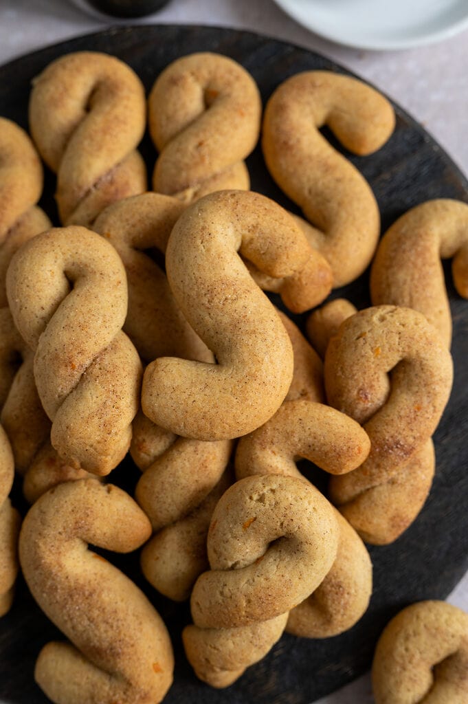 Olive oil koulourakia with orange and cinnamon on a brown wooden board.