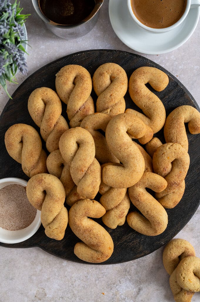 Olive oil koulourakia with orange and cinnamon on a brown wooden board.