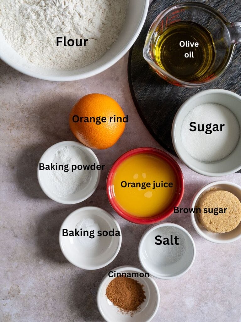 Ingredients for the olive oil koulourakia with orange and cinnamon which include: flour, olive oil, orange juice, orange zest, baking powder, baking soda, salt, cinnamon, sugar and brown sugar.