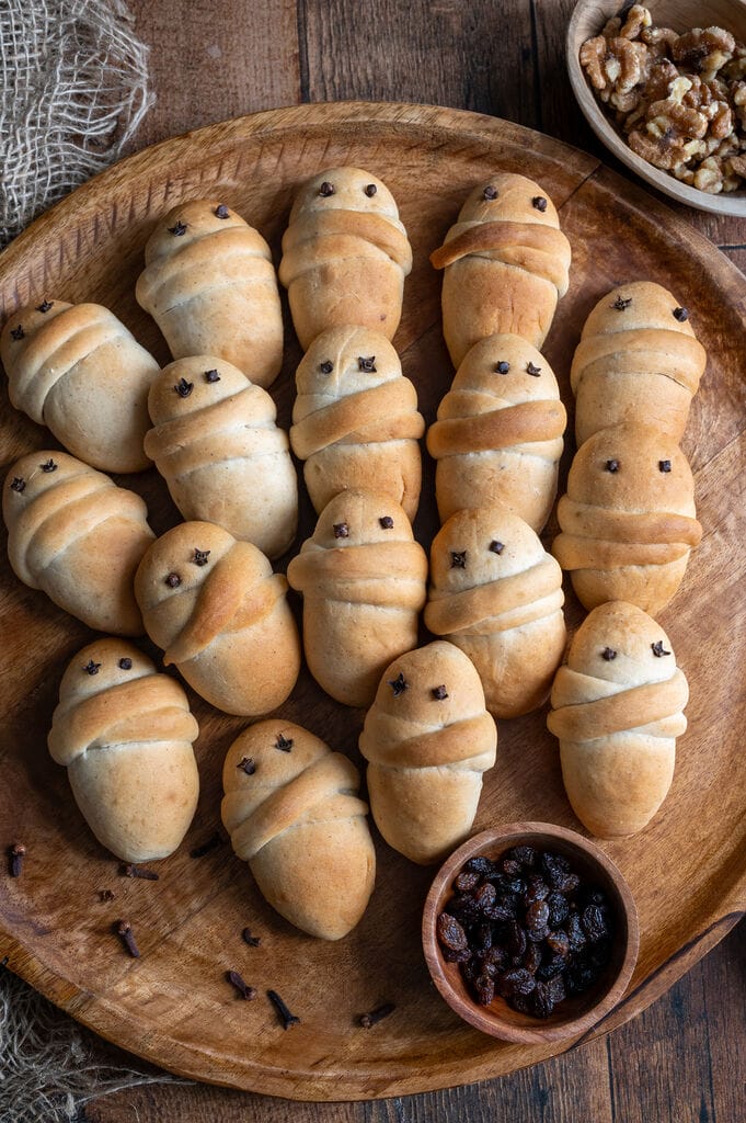 Lazarakia buns (Greek Easter Lazarus breads) on a wooden tray, surrounded by walnuts and raisins.
