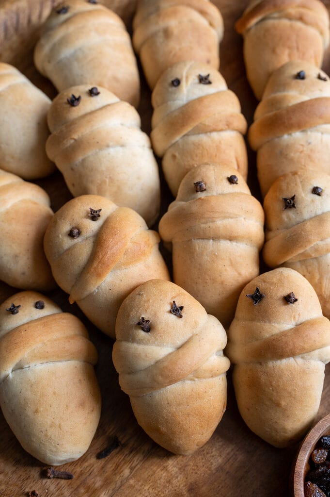 Lazarakia buns (Greek Easter Lazarus breads) on a wooden tray, surrounded by walnuts and raisins.