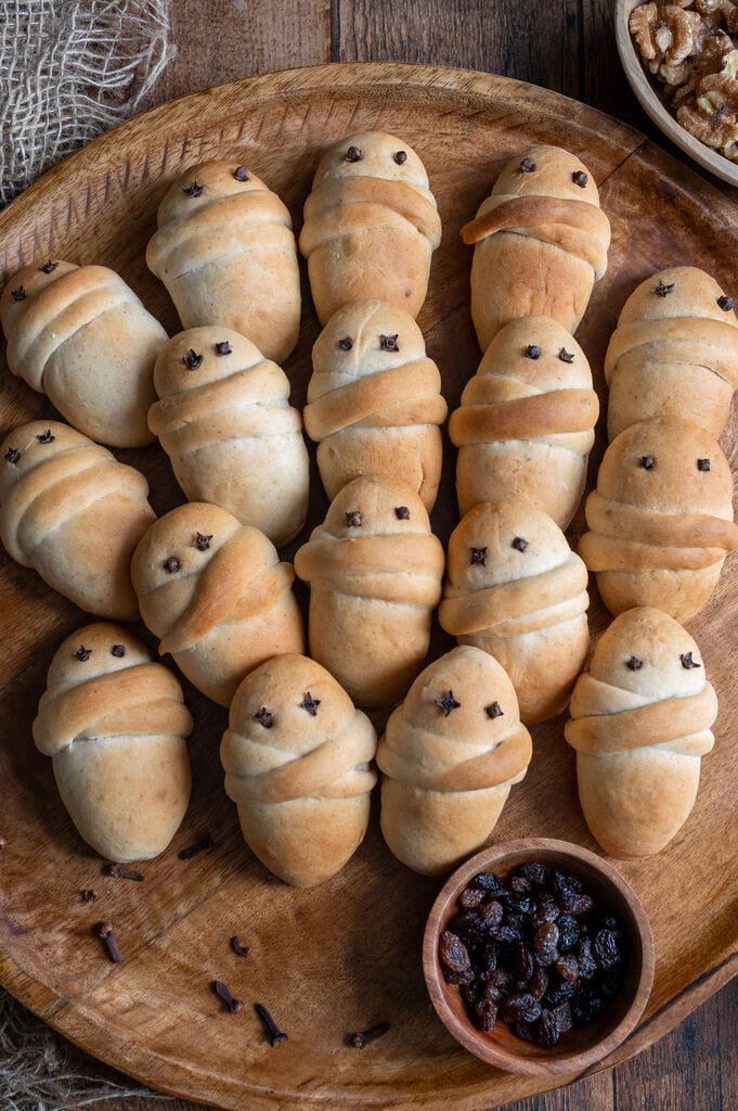 Lazarakia buns (Greek Easter Lazarus breads) on a wooden tray, surrounded by walnuts and raisins.