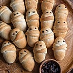 Lazarakia buns (Greek Easter Lazarus breads) on a wooden tray, surrounded by walnuts and raisins.