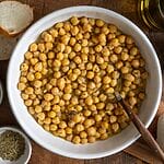 Baked chickpeas in a white bowl, surrounded by bread, and olives.