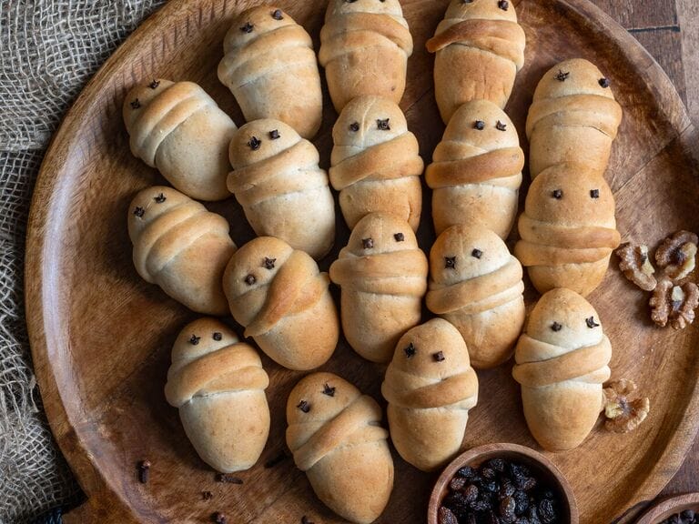 Lazarakia buns (Greek Easter Lazarus breads) on a wooden tray, surrounded by walnuts and raisins.