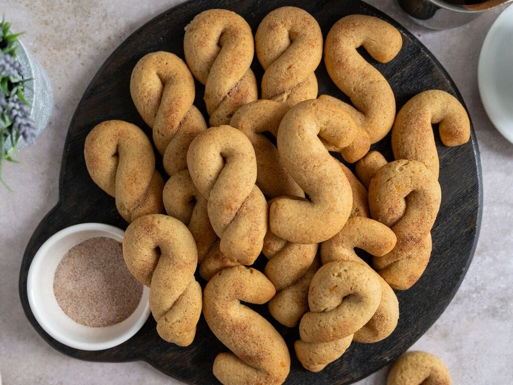Olive oil koulourakia with orange and cinnamon on a brown wooden board.