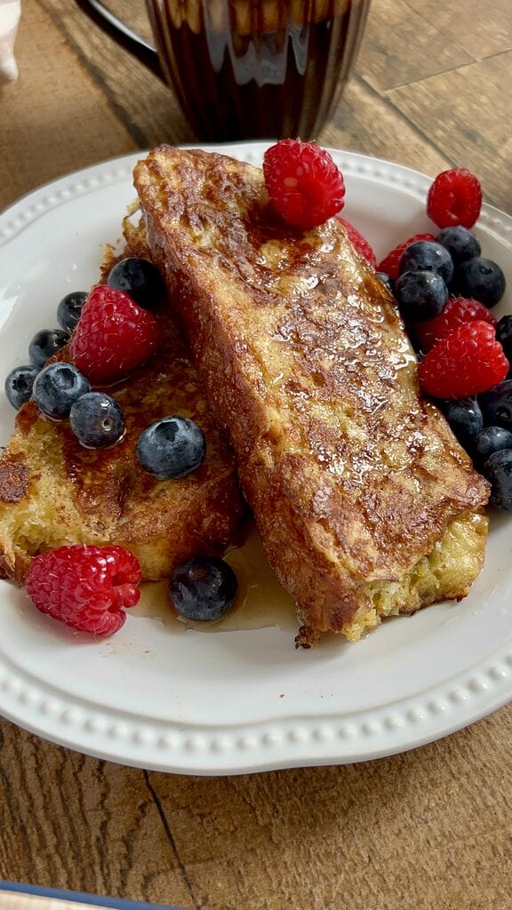 Tsoureki French toast, Greek Easter bread French toast on a white plate, surrounded by berries and topped with maple syrup.