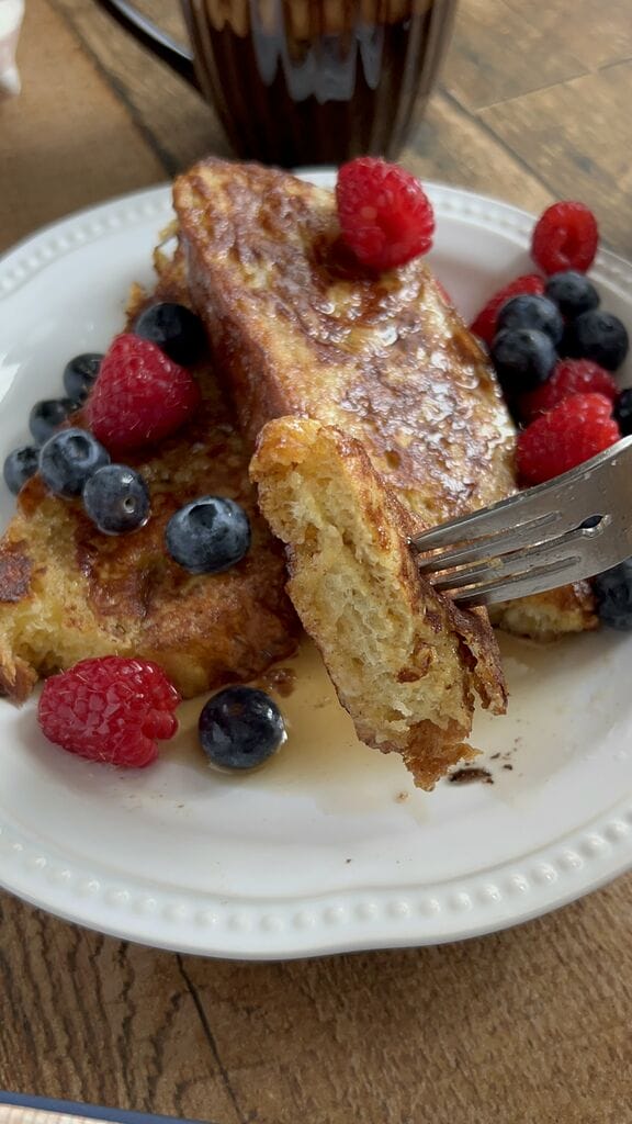 Tsoureki French toast, Greek Easter bread French toast on a white plate, surrounded by berries and topped with maple syrup.